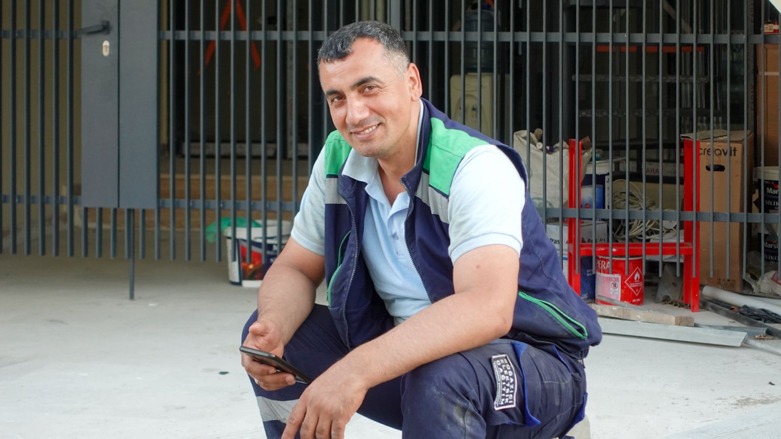 A construction worker holding a smartphone outside a building site.